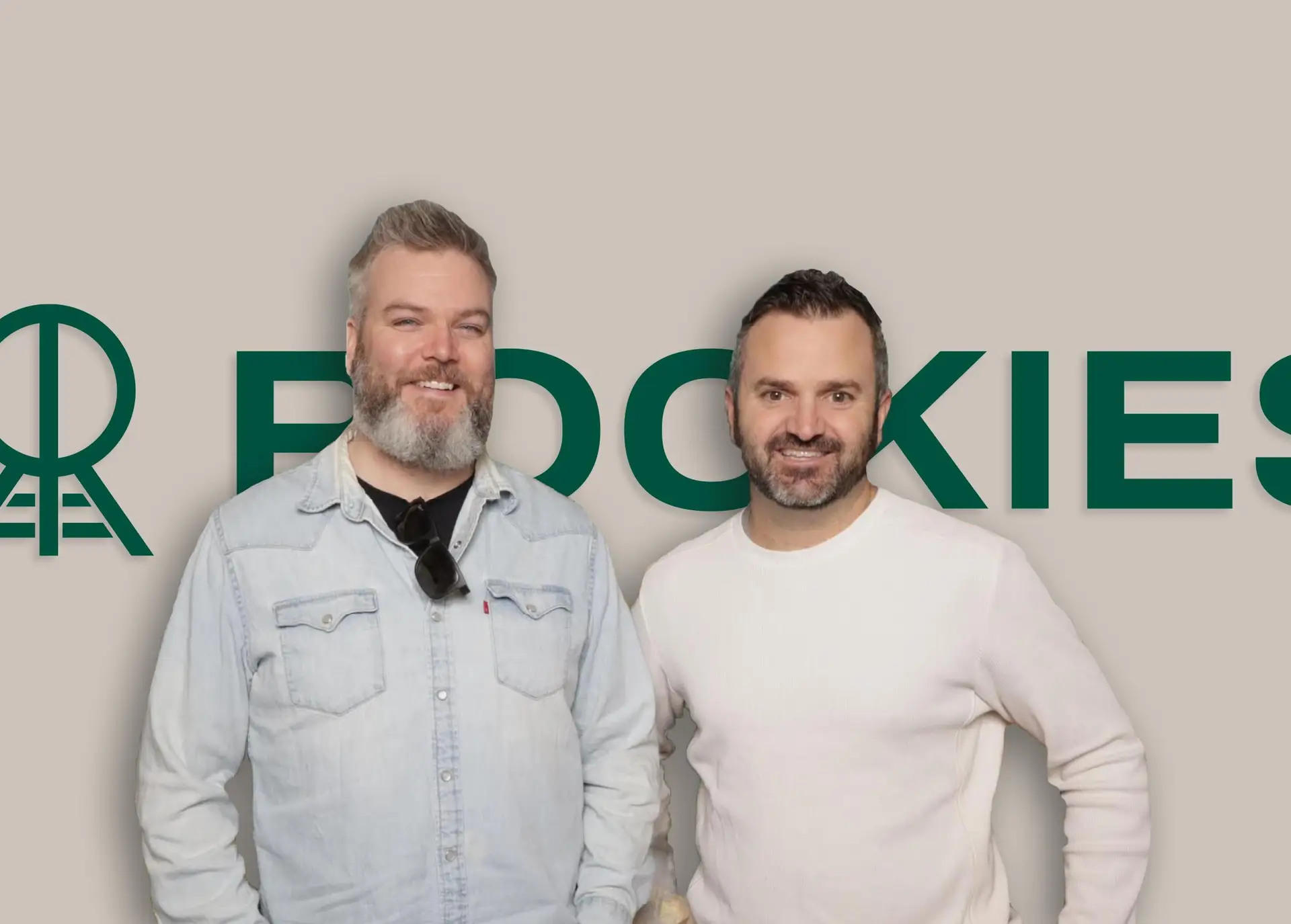 Two men smiling in front of a beige background with the word "ROOKIES" in green. One man has a beard and is wearing a denim jacket, while the other has shorter hair and is dressed in a white sweater.