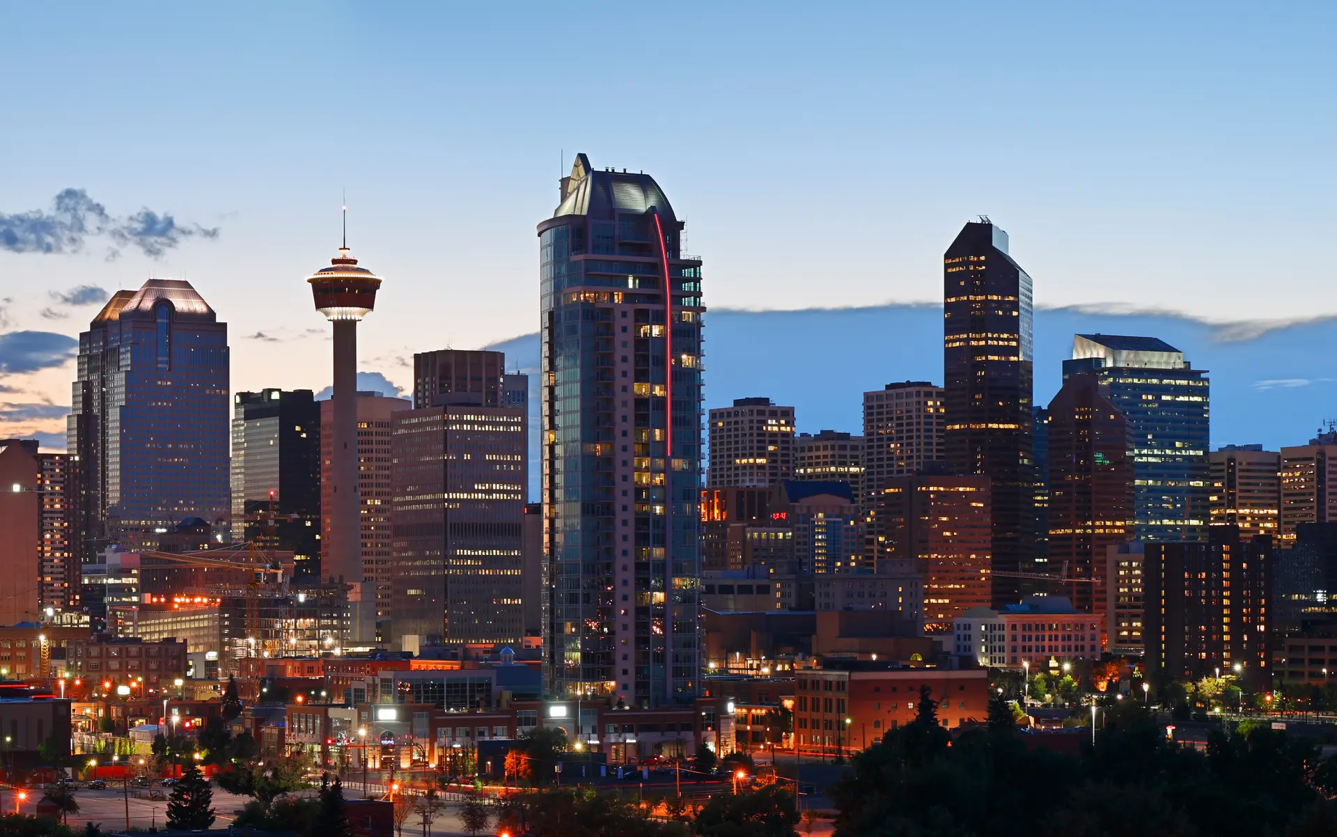 Calgary skyline at dusk featuring the iconic Calgary Tower, modern high-rise buildings, and illuminated streets, showcasing the vibrant cityscape and urban architecture.