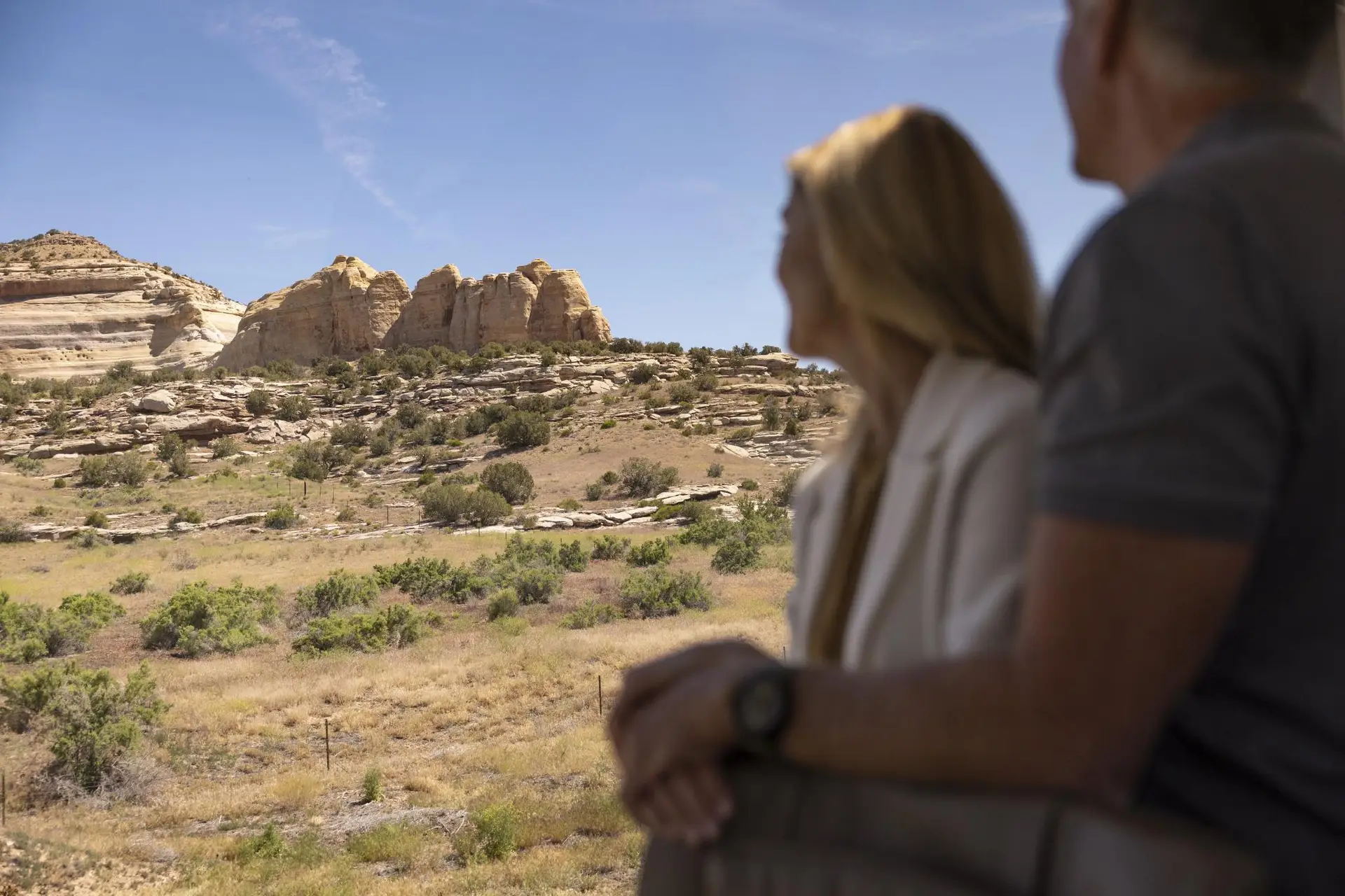 Couple enjoying a scenic view of rocky formations and greenery under a clear blue sky in a natural landscape.