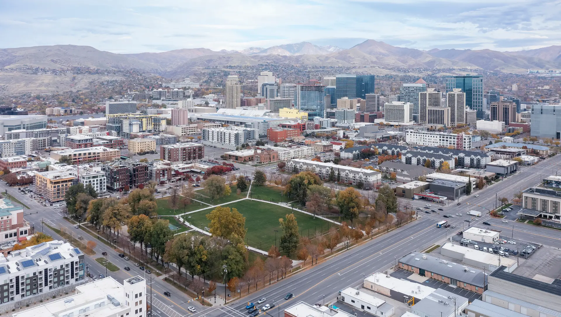 Aerial view of downtown Salt Lake City, showcasing a mix of modern skyscrapers and historic buildings, with the Wasatch Mountains in the background and a green park area in the foreground, highlighting the city's urban landscape and natural beauty.