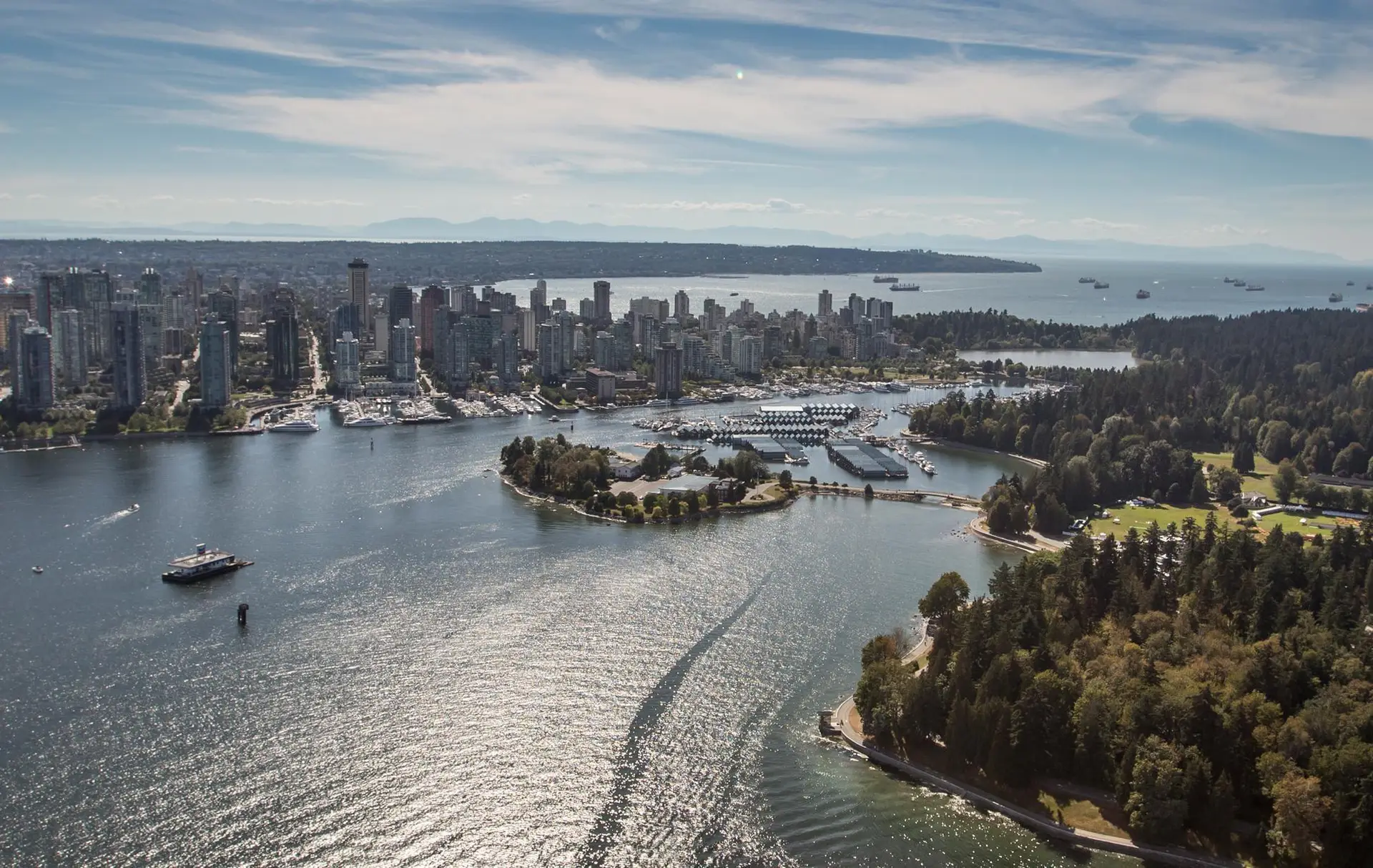 Aerial view of Vancouver, showcasing the skyline, waterfront, and surrounding greenery with boats in the harbor and mountains in the background. Ideal for highlighting urban and natural landscapes.