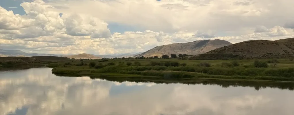 Scenic landscape featuring a tranquil river reflecting fluffy clouds and a blue sky, surrounded by lush green vegetation and rolling hills, ideal for nature photography and outdoor enthusiasts.