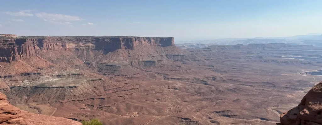 Vast desert landscape featuring red rock formations and canyons under a clear blue sky, showcasing the natural beauty of the American Southwest.