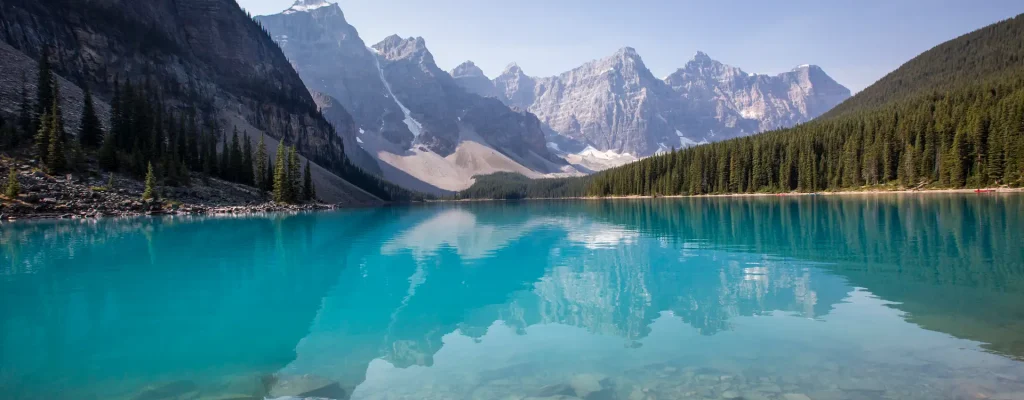 Stunning landscape of turquoise lake surrounded by majestic mountains and evergreen forest, reflecting the vibrant colors of nature under a clear blue sky.